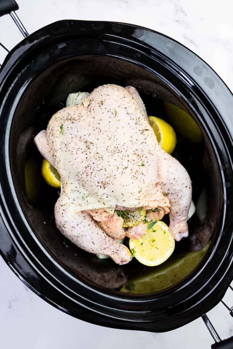 A whole chicken stuffed with lemon, onion, and herbs in a crockpot.