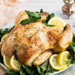 A whole lemon-roasted chicken on a serving platter with lemon slices.