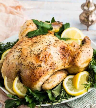A whole lemon-roasted chicken on a serving platter with lemon slices.