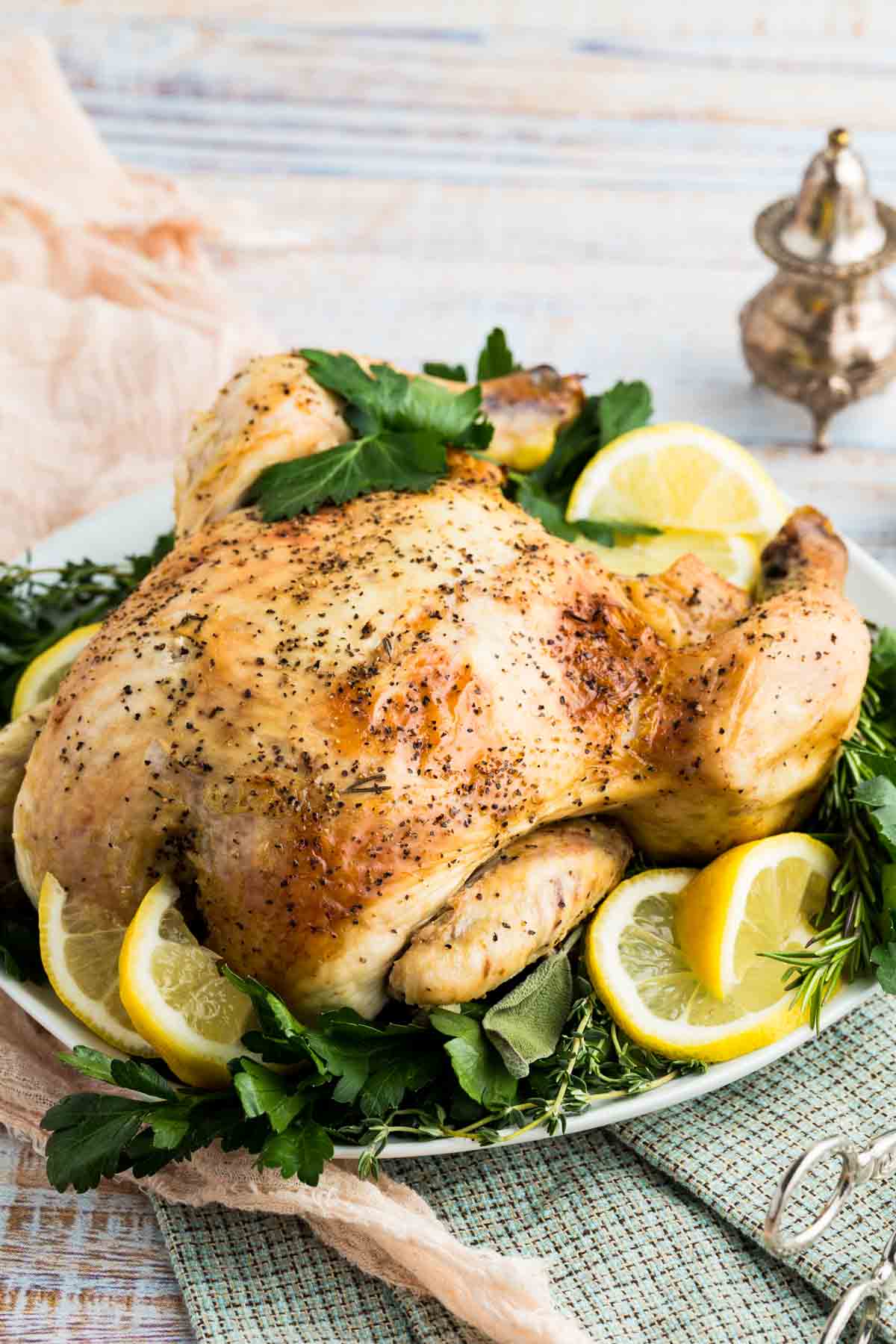 A whole lemon-roasted chicken on a serving platter with lemon slices.