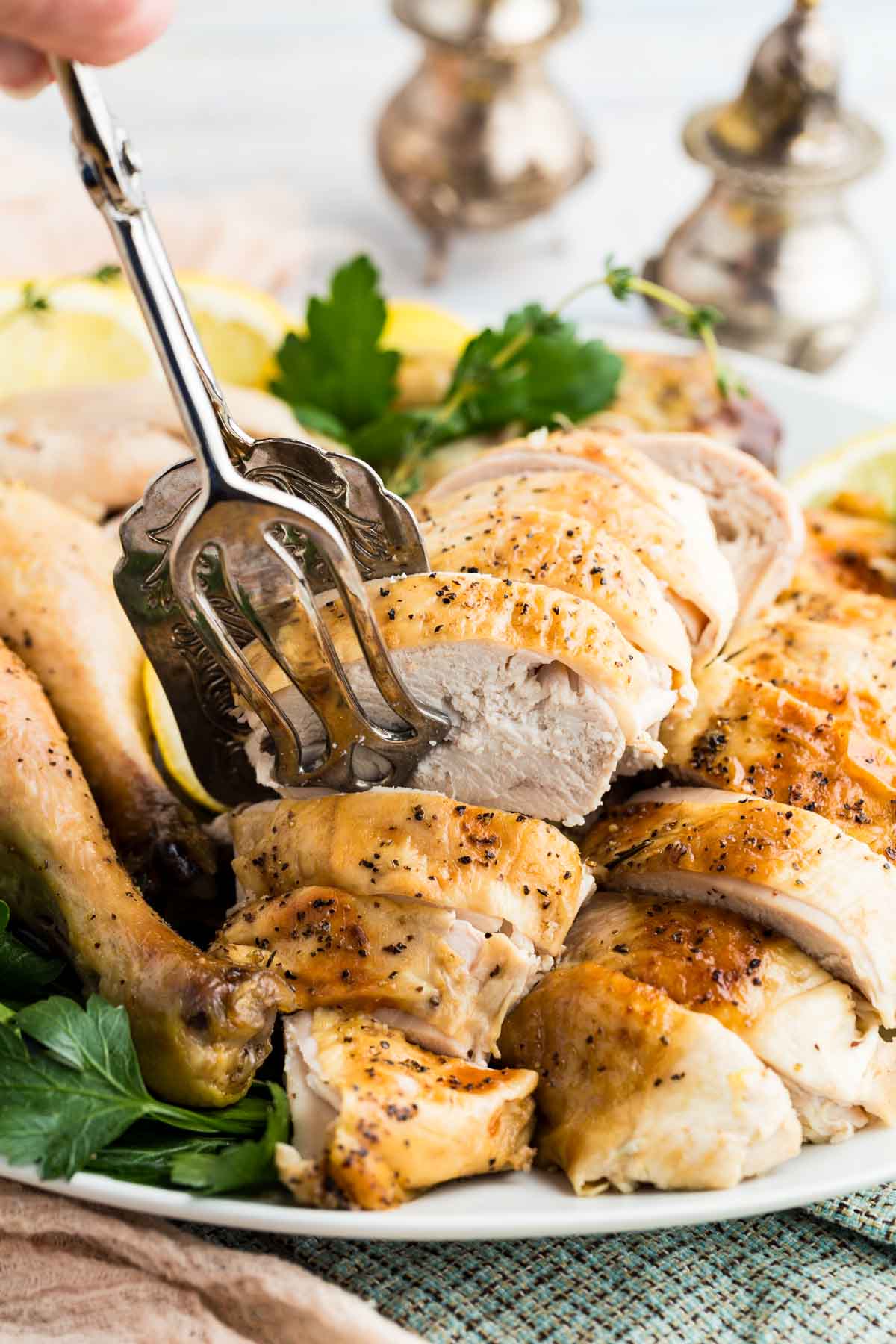 Serving tongs taking a couple of slices of lemon roast chicken breasts from a platter.