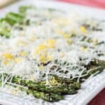 A platter of asparagus topped with shredded cheese and lemon zest with text overlay that says "Lemon Parmesan Grilled Asparagus".
