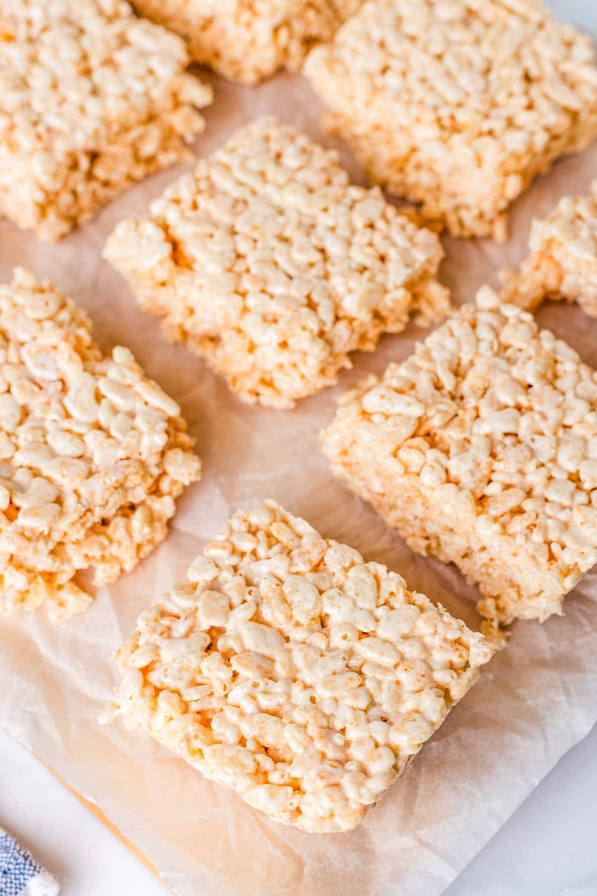 Rice krispie treats spread out on a sheet of parchment paper.