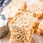 A stack of 3 rice krispie treats on a sheet of parchment paper with more rice krispie treats in the background.