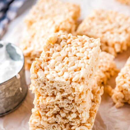 A stack of 3 rice krispie treats on a sheet of parchment paper with more rice krispie treats in the background.