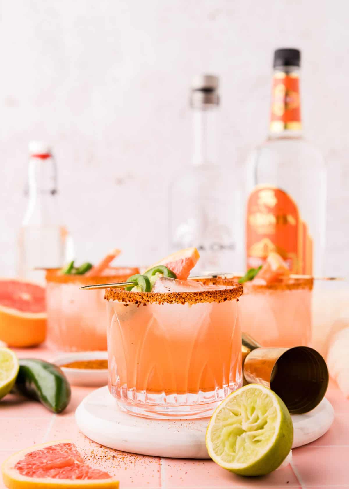 Spicy grapefruit margaritas with ingredients in the background.