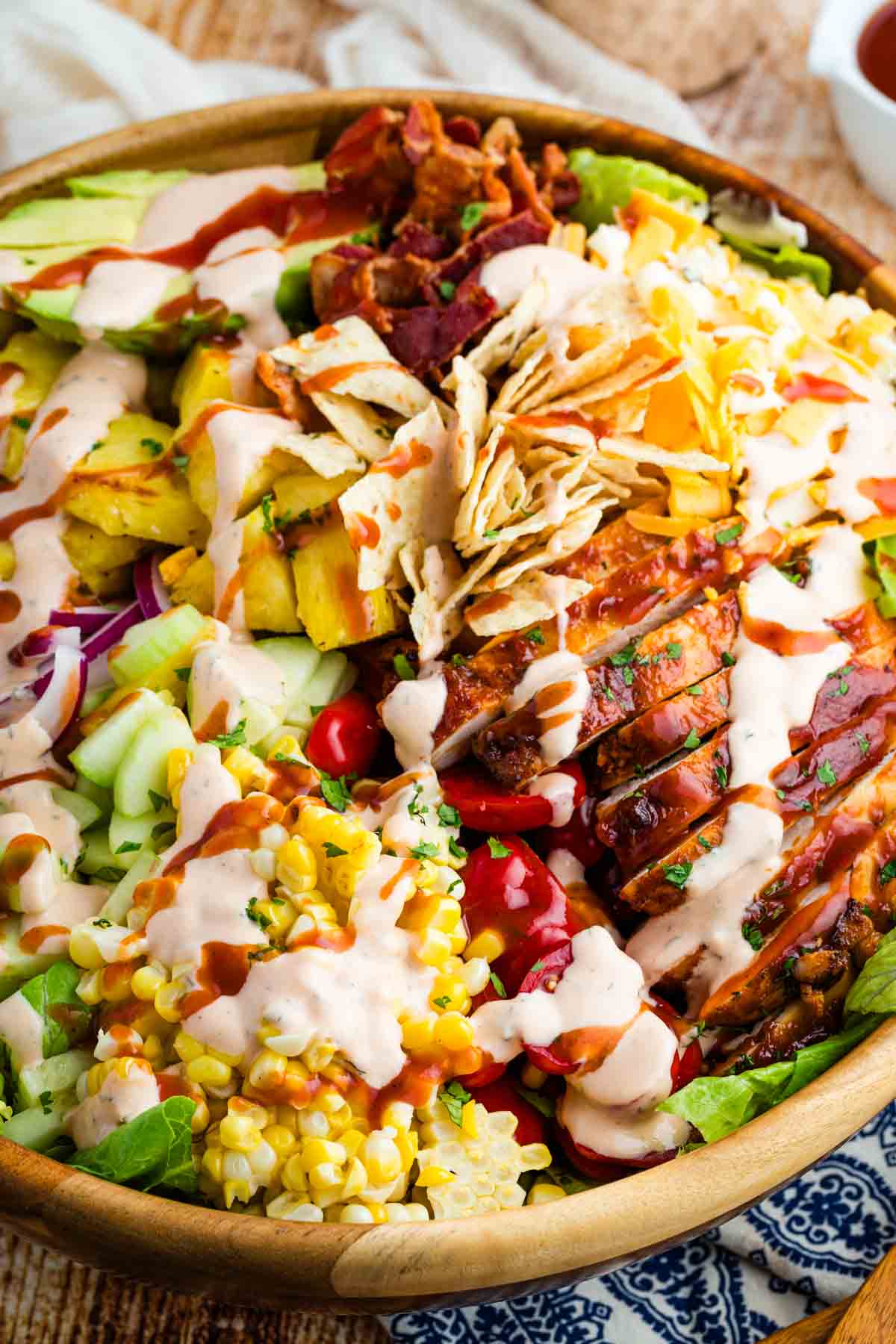 This BBQ chicken salad is loaded with BBQ chicken, crispy bacon, juicy pineapple, creamy avocado, and more. A sweet and savory masterpiece. Close-up image of BBQ chicken salad in a wooden salad bowl (before tossing).