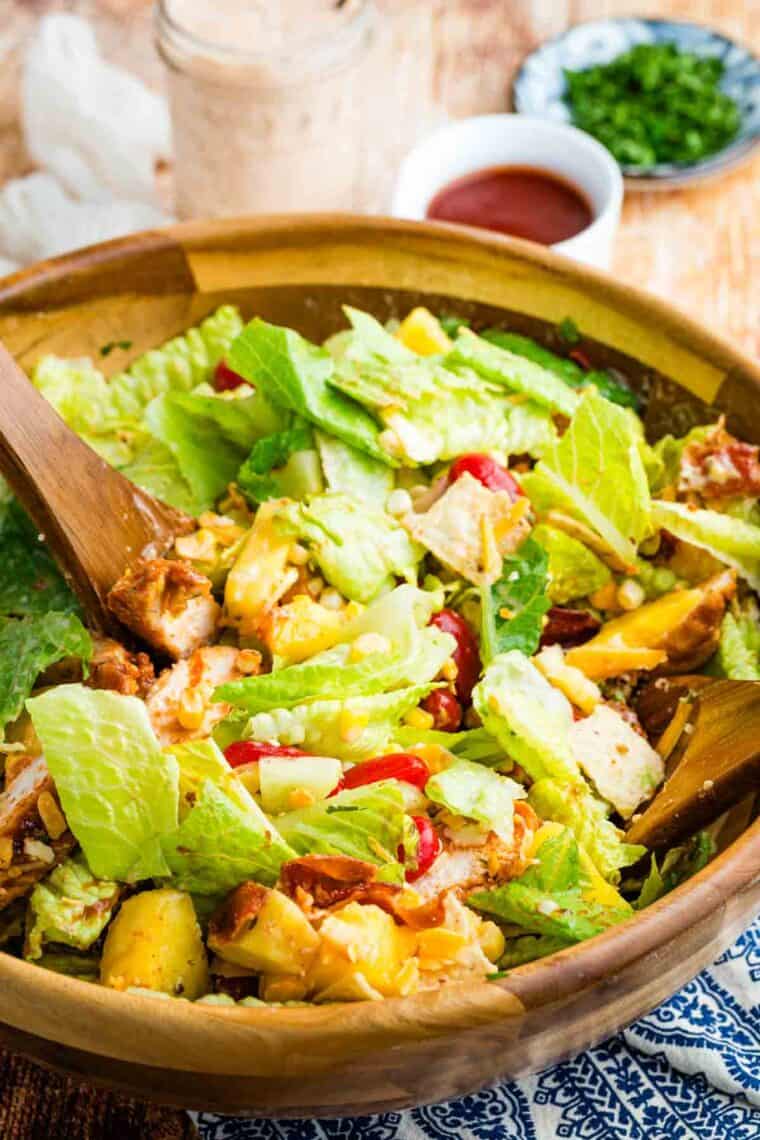 This BBQ chicken salad is loaded with BBQ chicken, crispy bacon, juicy pineapple, creamy avocado, and more. A sweet and savory masterpiece. Tossing BBQ chicken salad in a wooden salad bowl.