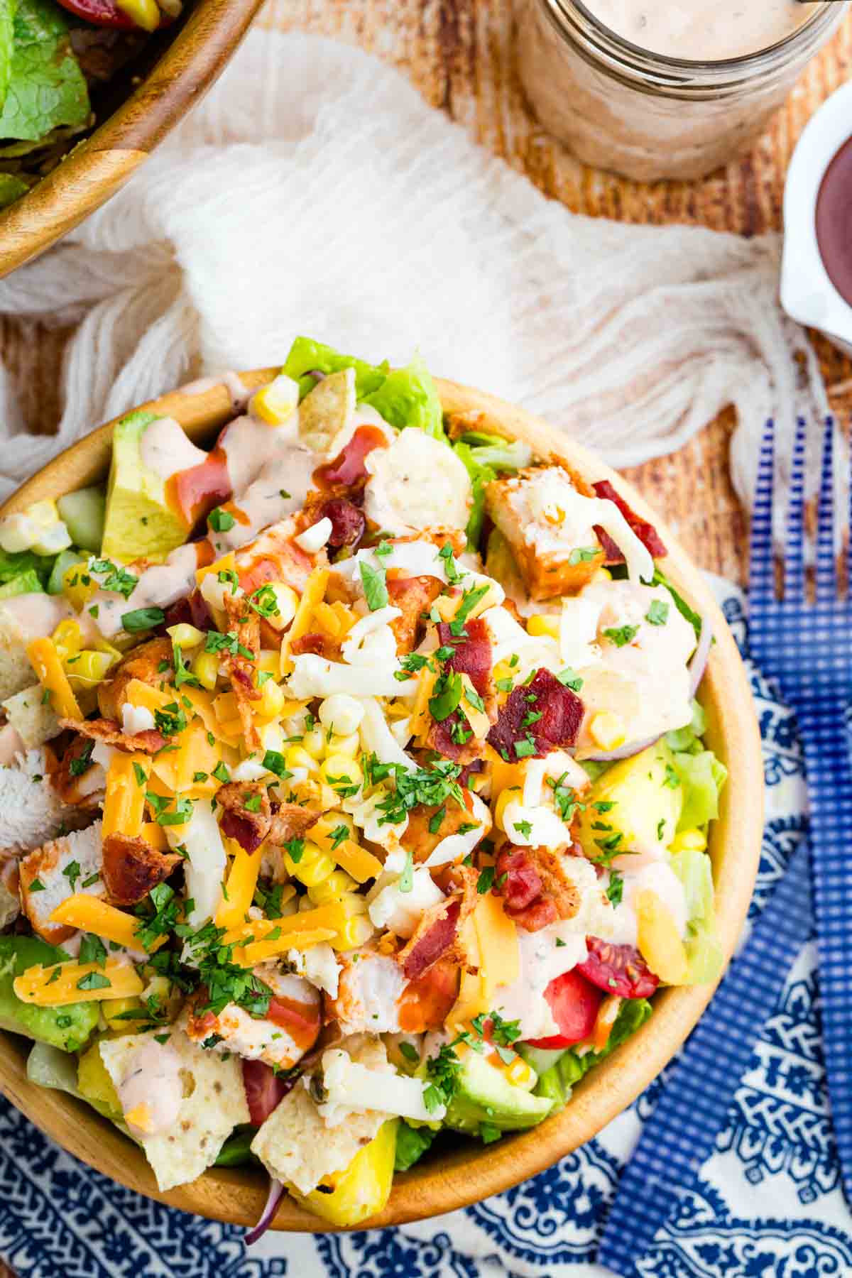 This BBQ chicken salad is loaded with BBQ chicken, crispy bacon, juicy pineapple, creamy avocado, and more. A sweet and savory masterpiece. Overhead image of a wooden bowl loaded with BBQ chicken salad.
