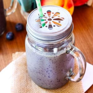 A blueberry peach smoothie in a glass with a metal cap on it.