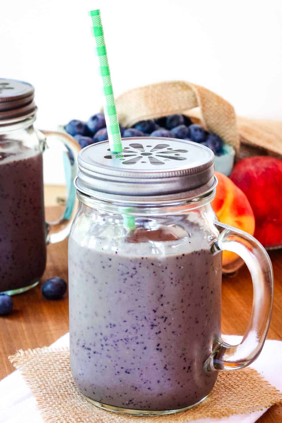 A blueberry peach smoothie in a glass with a handle and a cap.