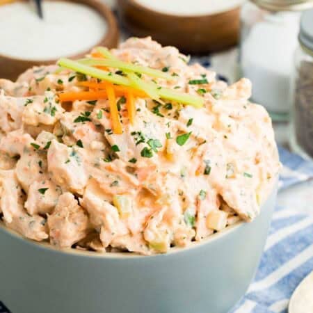 Buffalo chicken salad in a bowl, topped with tiny carrot and celery sticks.