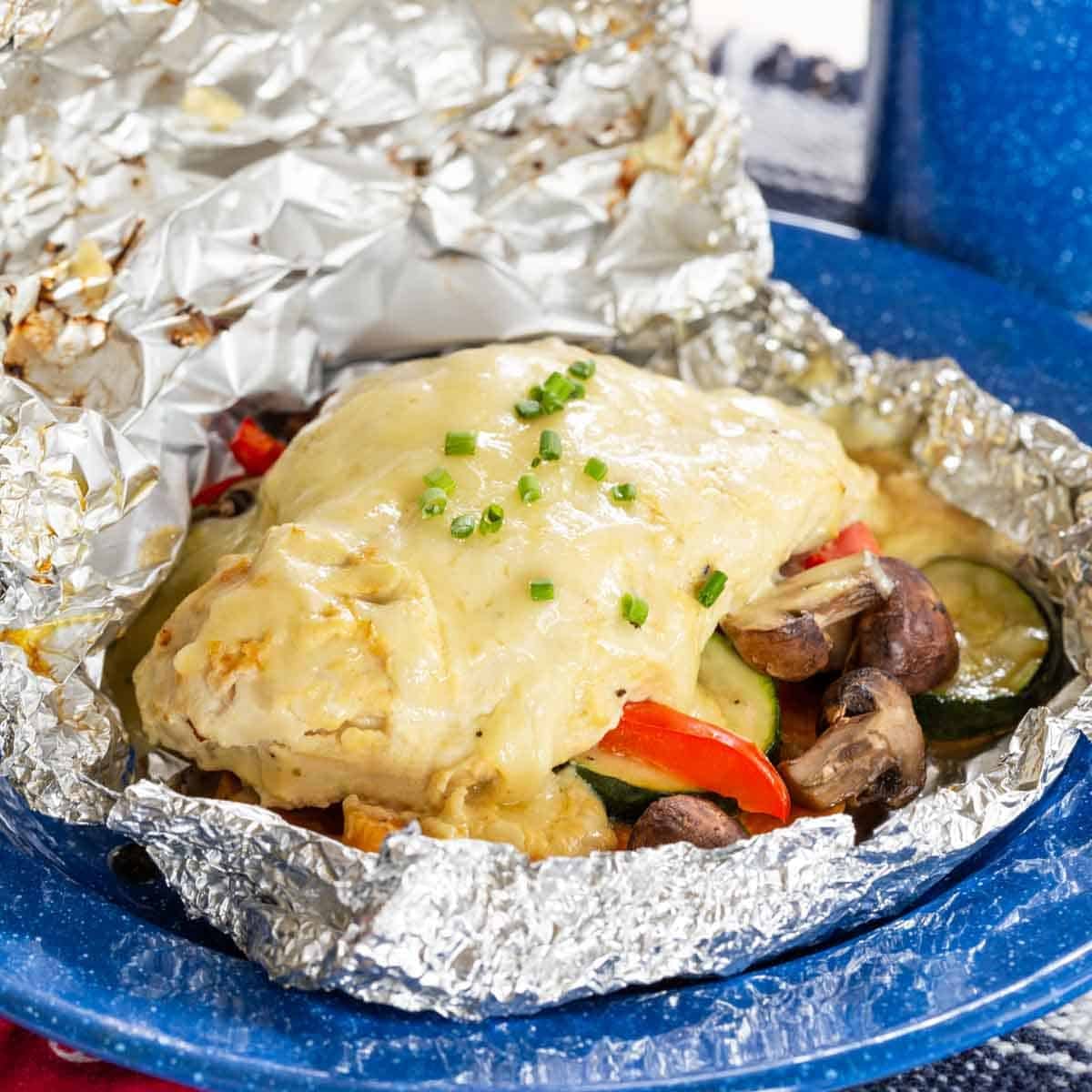 A chicken foil packet with vegetables and cheese on top on a blue plate.