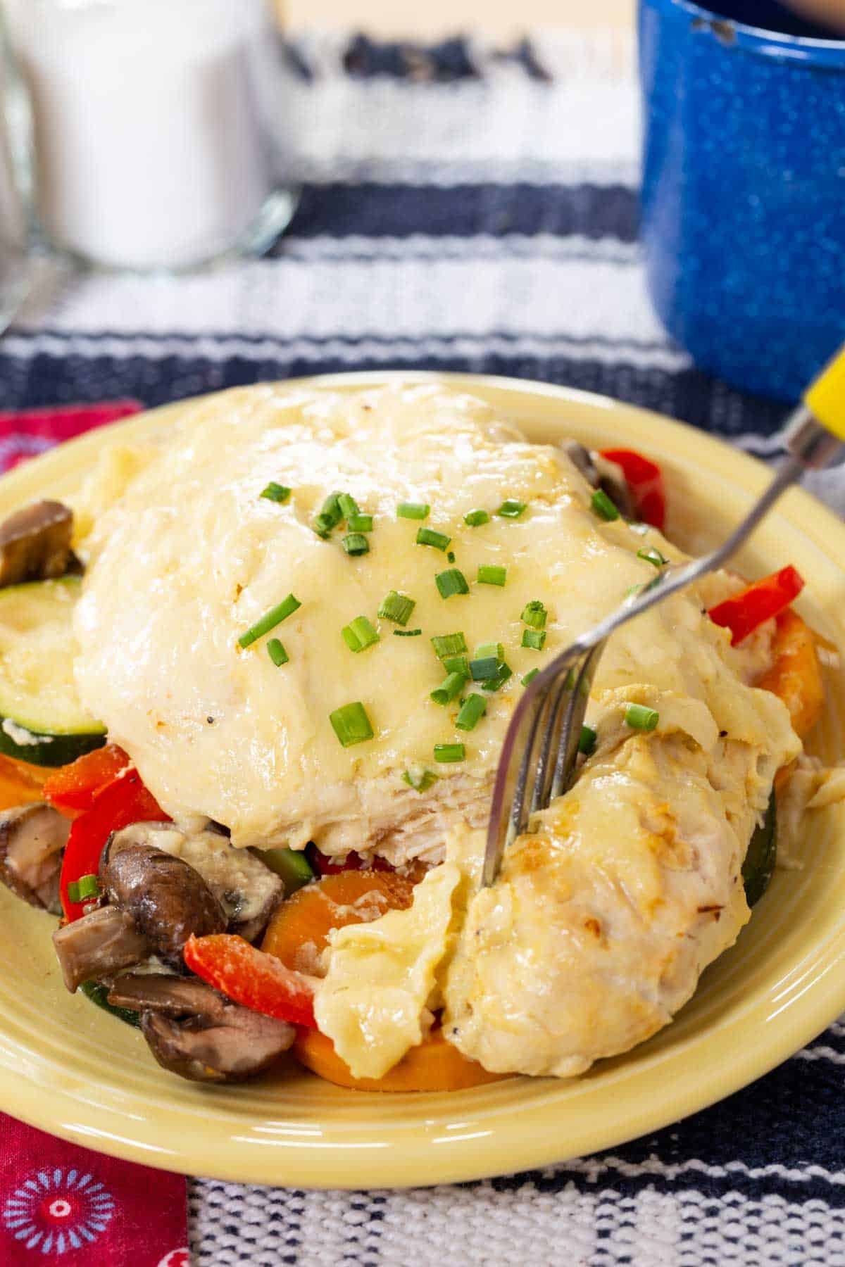A fork in a piece of chicken breast on top of a bed of veggies on a yellow plate.