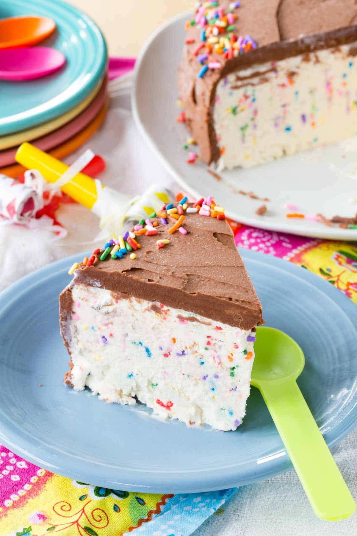 A piece of ice cream cake with rainbow sprinkles and a plastic spoon on a plate.