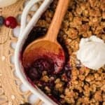 A wooden spoon in a gluten-free berry crisp with ice cream on top.
