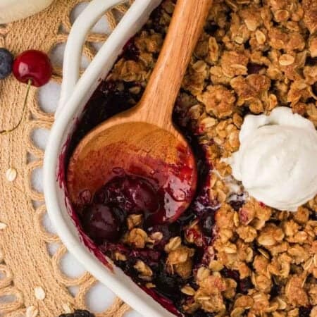 A wooden spoon in a gluten-free berry crisp with ice cream on top.