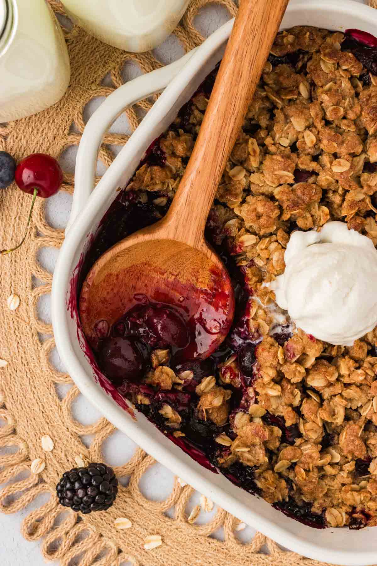 This summery gluten-free berry crisp is packed with jammy berries and topped with a buttery, cinnamon-y crumble that’s almost too good! A wooden spoon in a gluten-free berry crisp with ice cream on top.