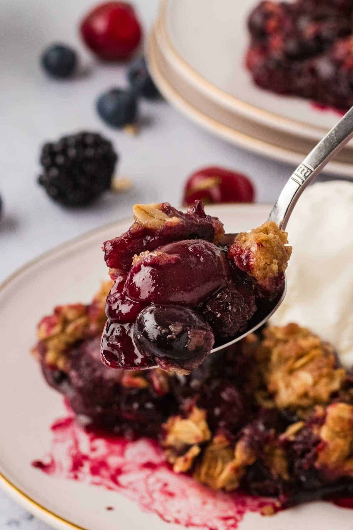 A spoon holding a bite of berry crisp up to the camera.