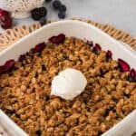 A baked fruit crisp in a casserole dish topped with a scoop of vanilla ice cream with text overlay that says "Gluten Free Berry Crisp".