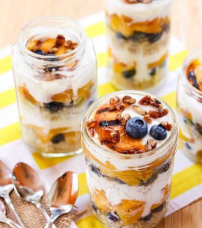 Peach blueberry yogurt parfaits in jars on a striped napkin.