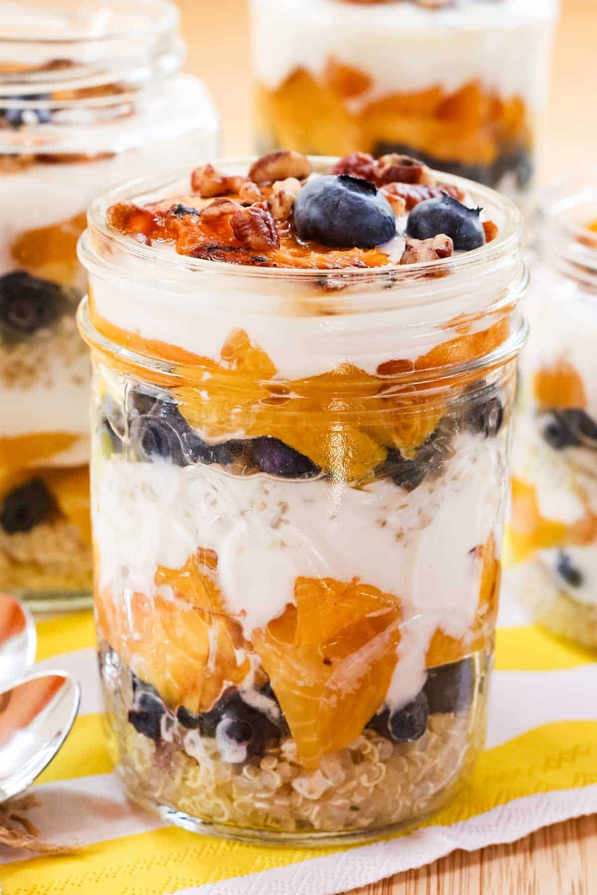 A grilled peach parfait in a glass jar with blueberries and yogurt and quinoa layers.