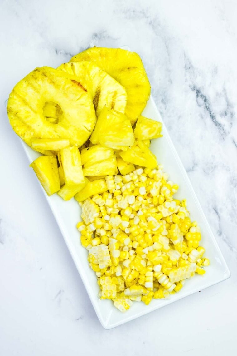 This BBQ chicken salad is loaded with BBQ chicken, crispy bacon, juicy pineapple, creamy avocado, and more. A sweet and savory masterpiece. Grilled pineapple rings and chunks on a plate with grilled corn off the cob.
