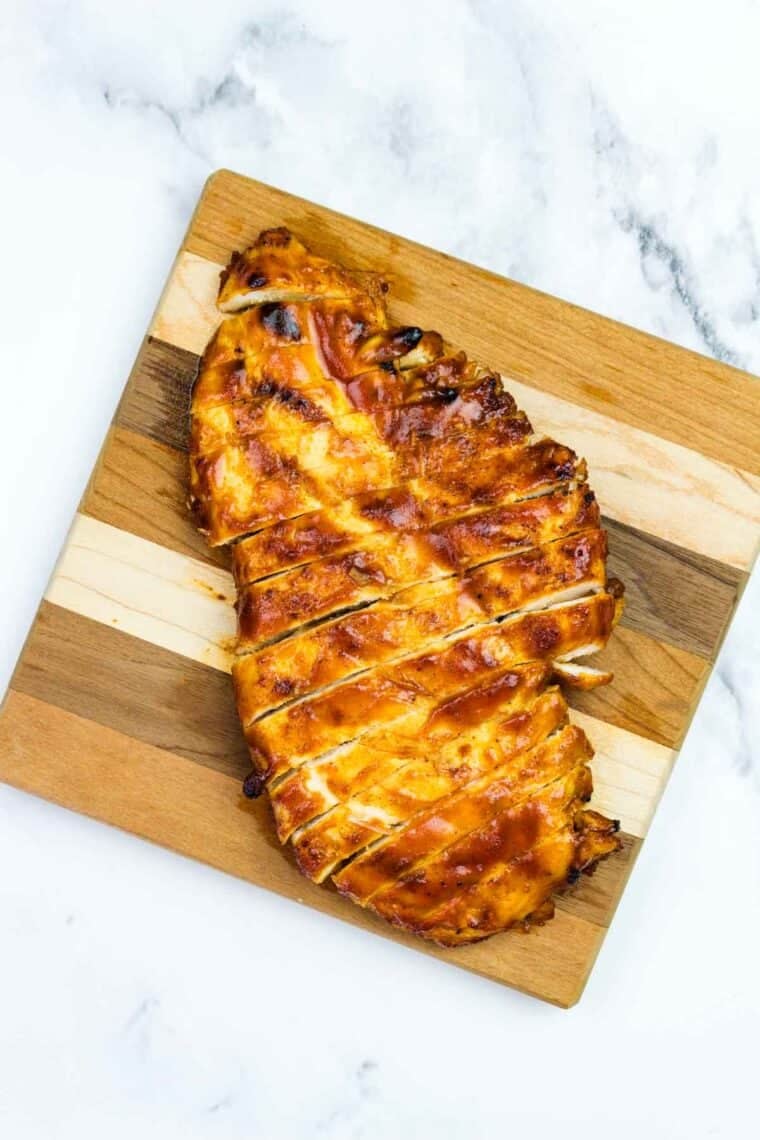 This BBQ chicken salad is loaded with BBQ chicken, crispy bacon, juicy pineapple, creamy avocado, and more. A sweet and savory masterpiece. Grilled BBQ chicken sliced on a cutting board.