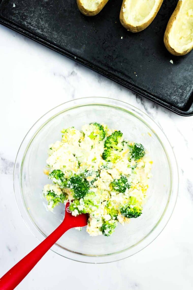 Mixing steamed broccoli, cheddar cheese, sour cream, chives, and salt into mashed potatoes.