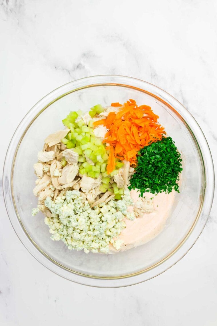 This flavor-packed Buffalo Chicken Salad is made with bold Greek yogurt dressing, tender chicken, crunchy veggies, and blue cheese. Yum! Adding shredded chicken, veggies, parsley, and blue cheese to a bowl of buffalo dressing.