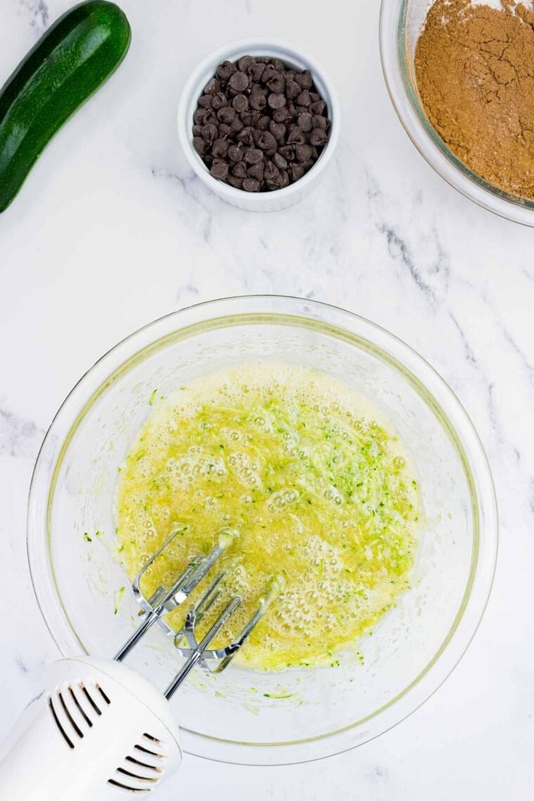 These gluten-free chocolate zucchini muffins are packed with melty chocolate chips and incredibly moist and tender, thanks to the zucchini. Mixing zucchini into maple syrup, oil, applesauce, granulated sugar, eggs, and vanilla extract.