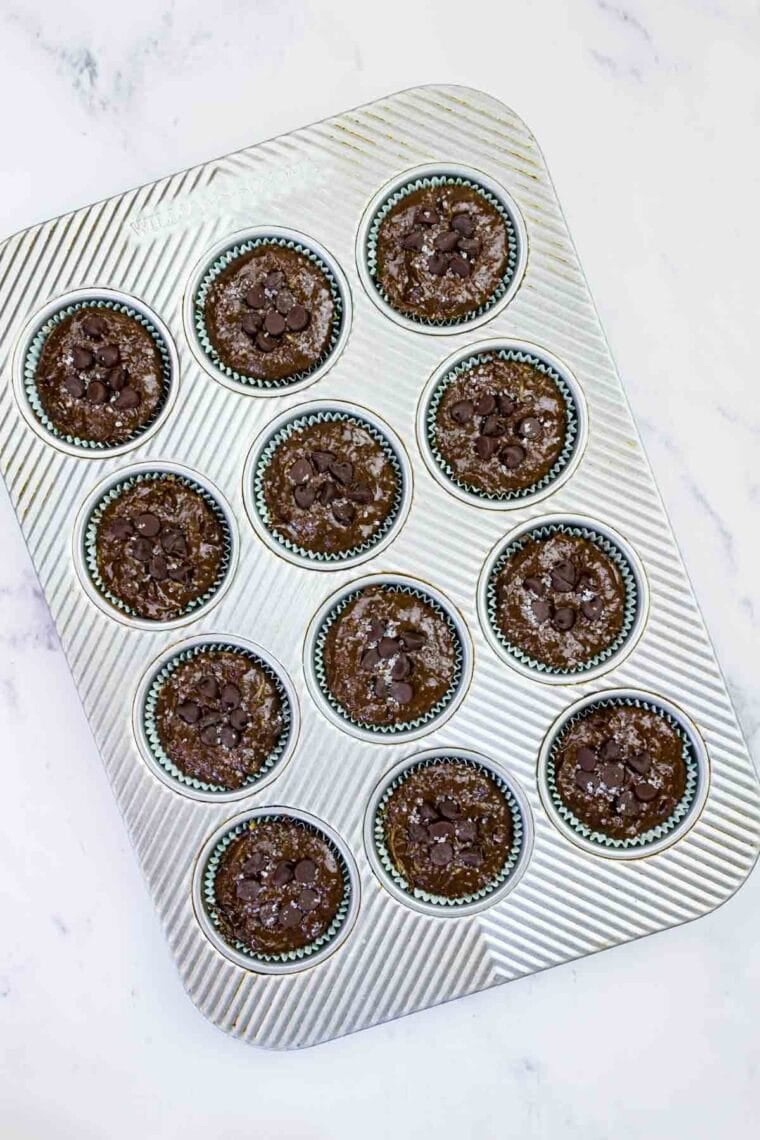 These gluten-free chocolate zucchini muffins are packed with melty chocolate chips and incredibly moist and tender, thanks to the zucchini. GF chocolate zucchini muffin batter topped with chocolate chips in muffin tins.