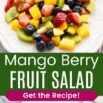 A platter of chopped strawberries, kiwi, mango, and blueberries and some in a wooden spoon divided by a green box with text overlay that says "Mango Berry Fruit Salad" and the words "Get the Recipe!".