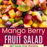 A wooden spoon picking up chopped strawberries, kiwi, mango, and blueberries and the fruit on a platter divided by a red box with text overlay that says "Mango Berry Fruit Salad" and the words "with honey lime dressing".