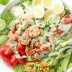 A bowl of lettuce topped with shrimp, corn, tomatoes, bacon, and hard boiled eggs with text overlay that says "Southwest Shrimp Salad".