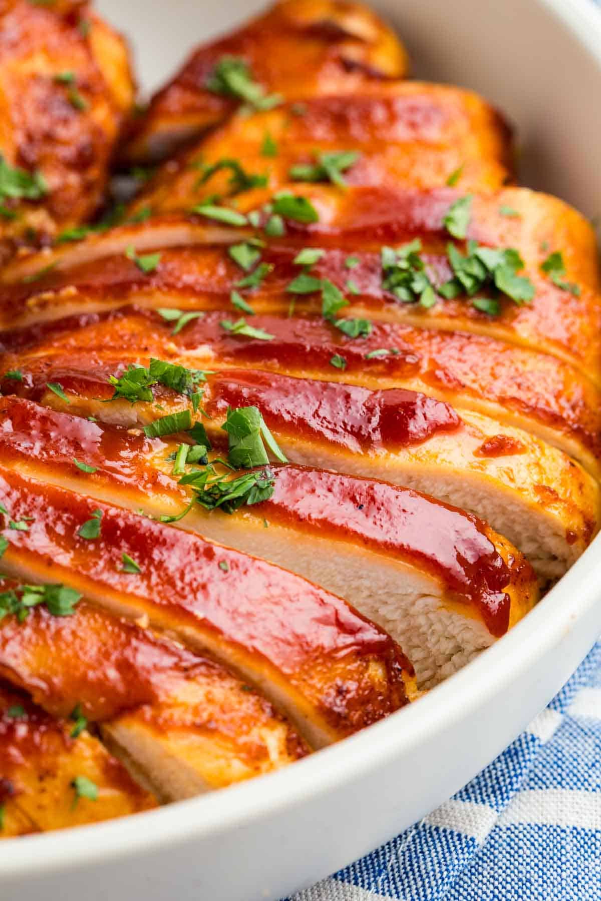 Close-up image of sliced BBQ chicken breasts in a white bowl.