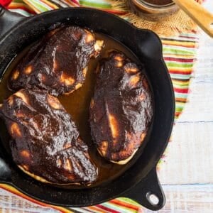 Three chicken breasts covered with barbecue sauce in a cast iron skillet.