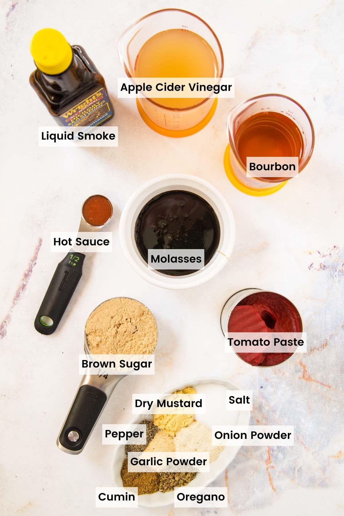Bowls and measuring cups with tomato paste, bourbon, apple cider vinegar, brown sugar, molasses, hot sauce, and different spices and seasonings, and a bottle of liquid smoke with text labels.