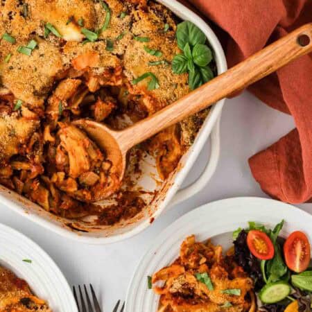 Overhead image of eggplant casserole in a baking dish next to a plate loaded with a serving of eggplant casserole and salad.