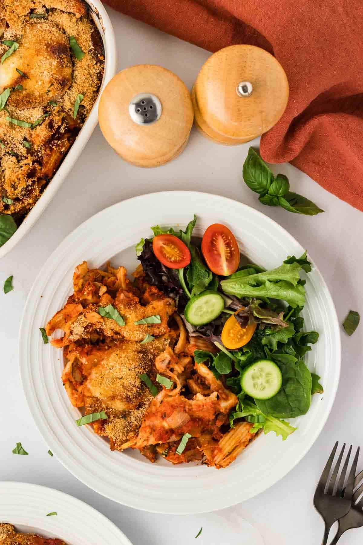 Overhead image of a serving of eggplant casserole on a plate with salad.