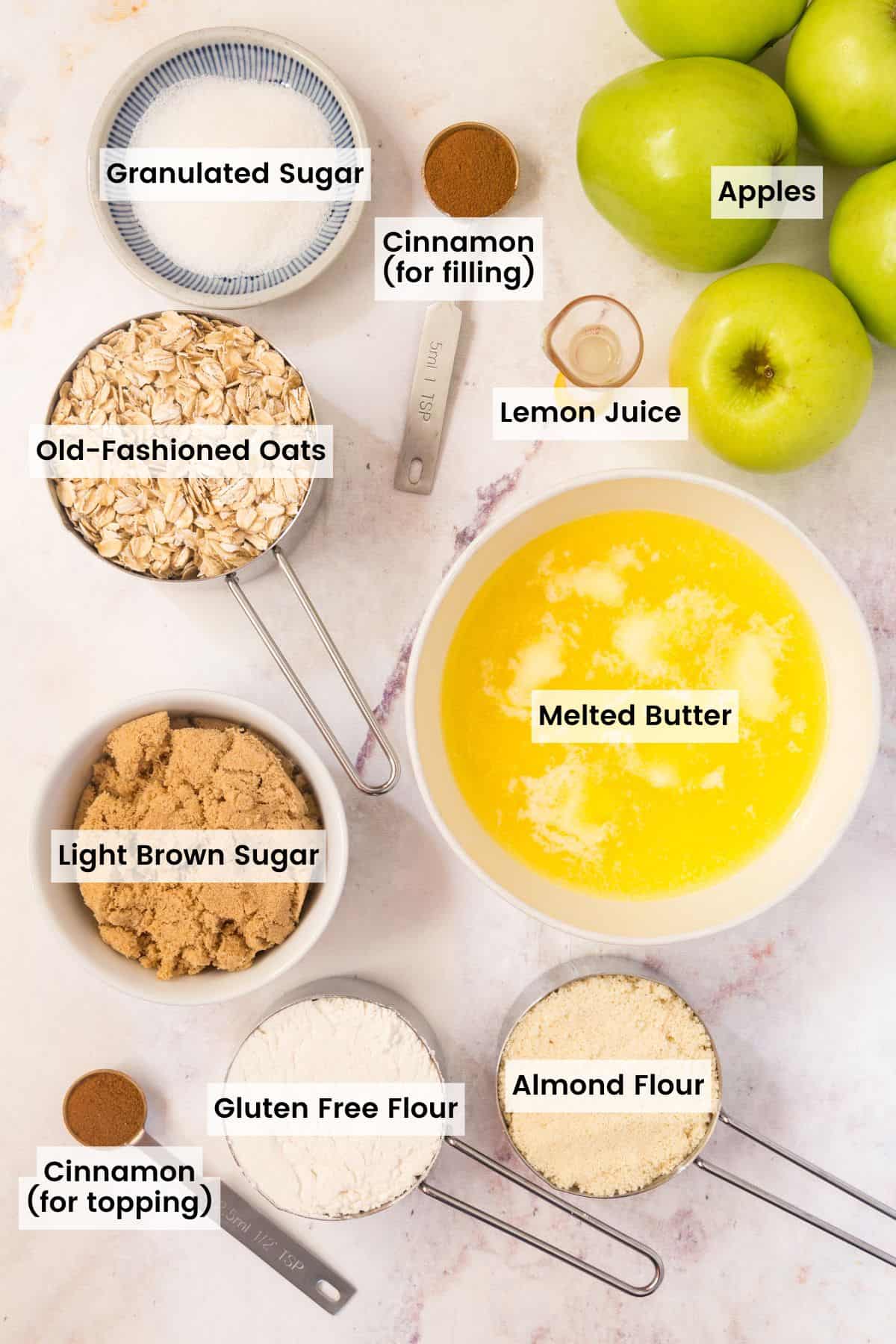 Ingredients to make a gluten free apple crisp with some green apples on a marble countertop with text labels.