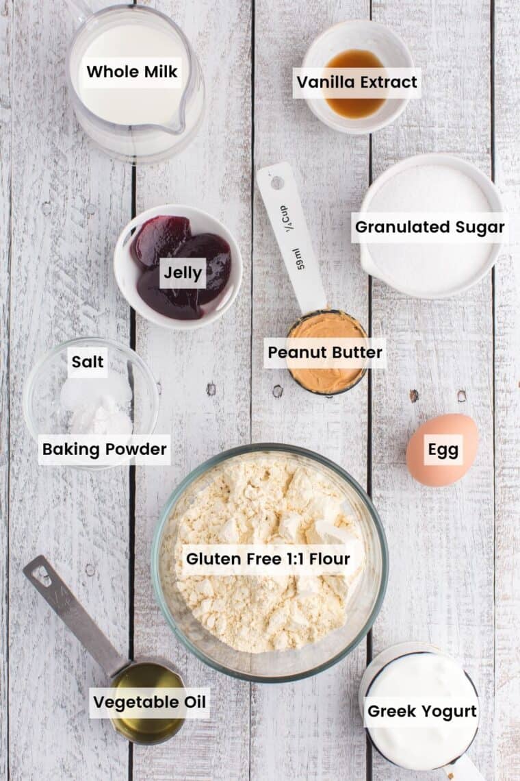 Bowls of gluten free flour, salt, baking powder, sugar and vanilla extract, a pitcher of milk, and measuring cups with peanut butter, yogurt, and oil with text labels.