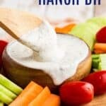 A wooden spoon in a bowl of dip surrounded by veggies with text overlay that says "Greek Yogurt Ranch Dip".
