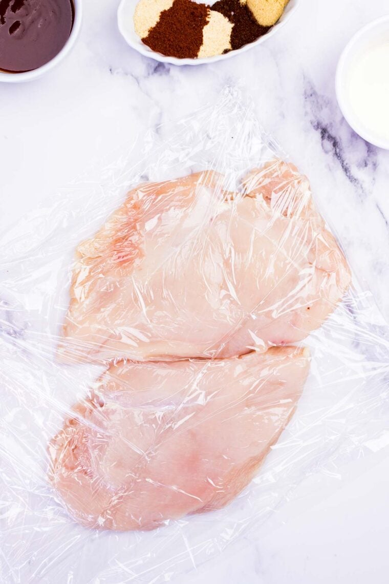 Two chicken breasts between sheets of plastic.