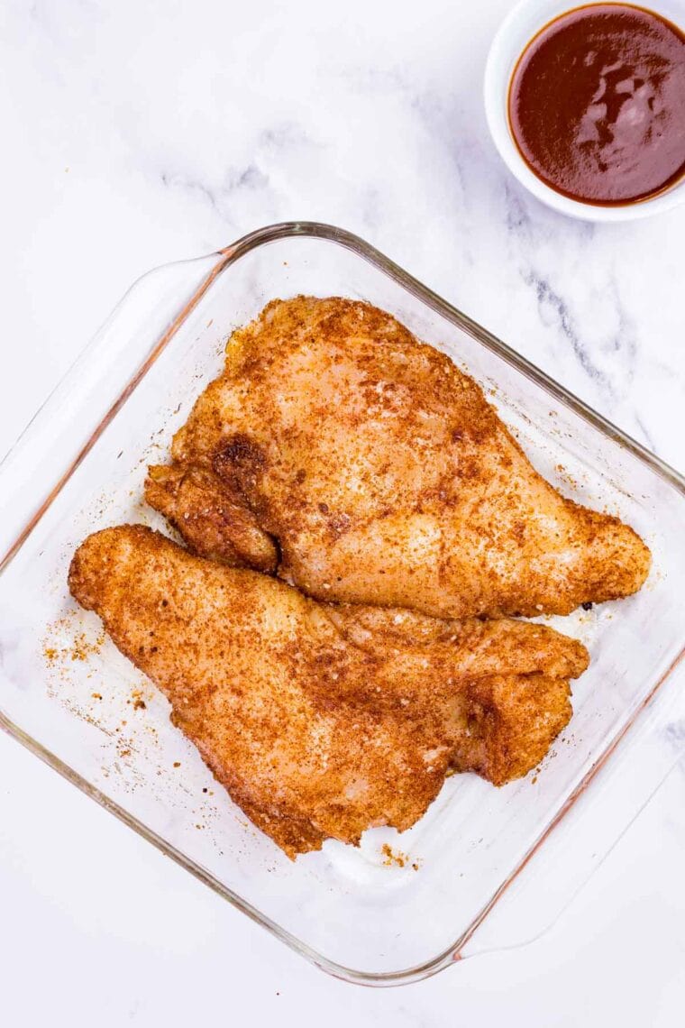 Seasoned chicken breasts in a glass container.