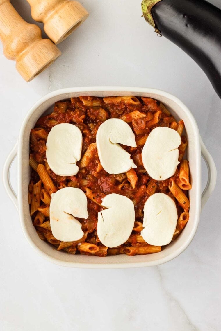 Layering slices of fresh mozzarella over saucy eggplant pasta in a casserole dish.
