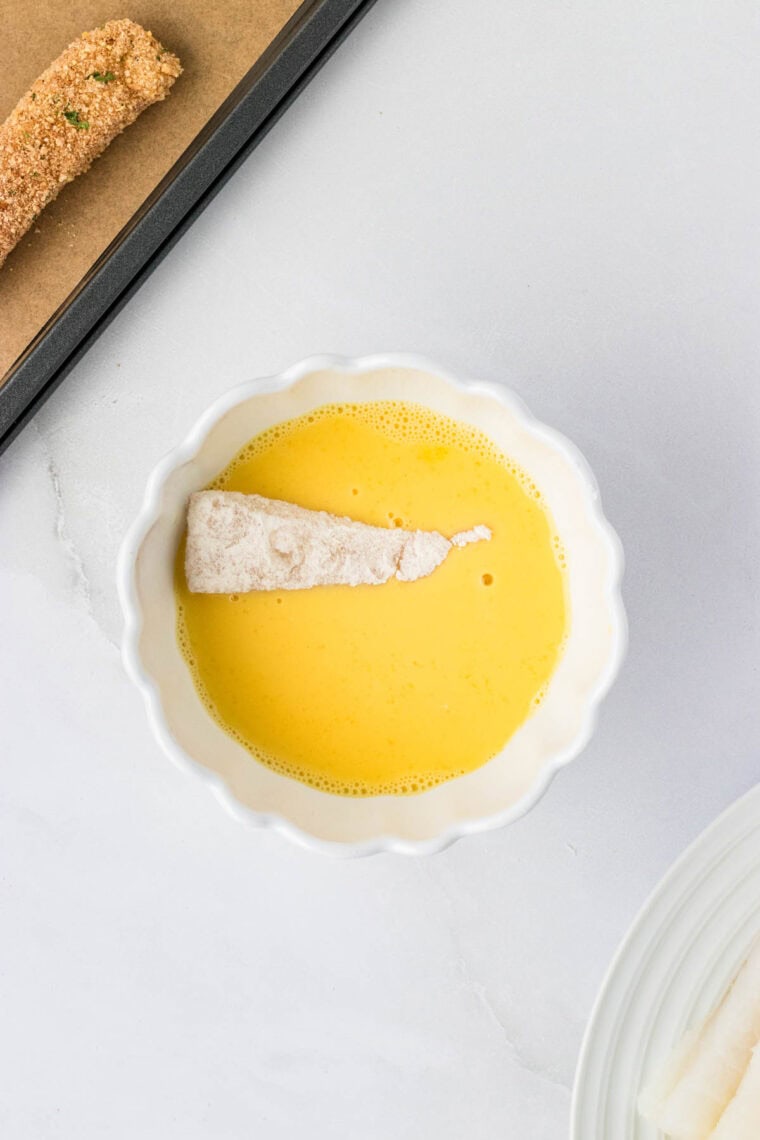 Dipping a piece of floured cod in egg wash.