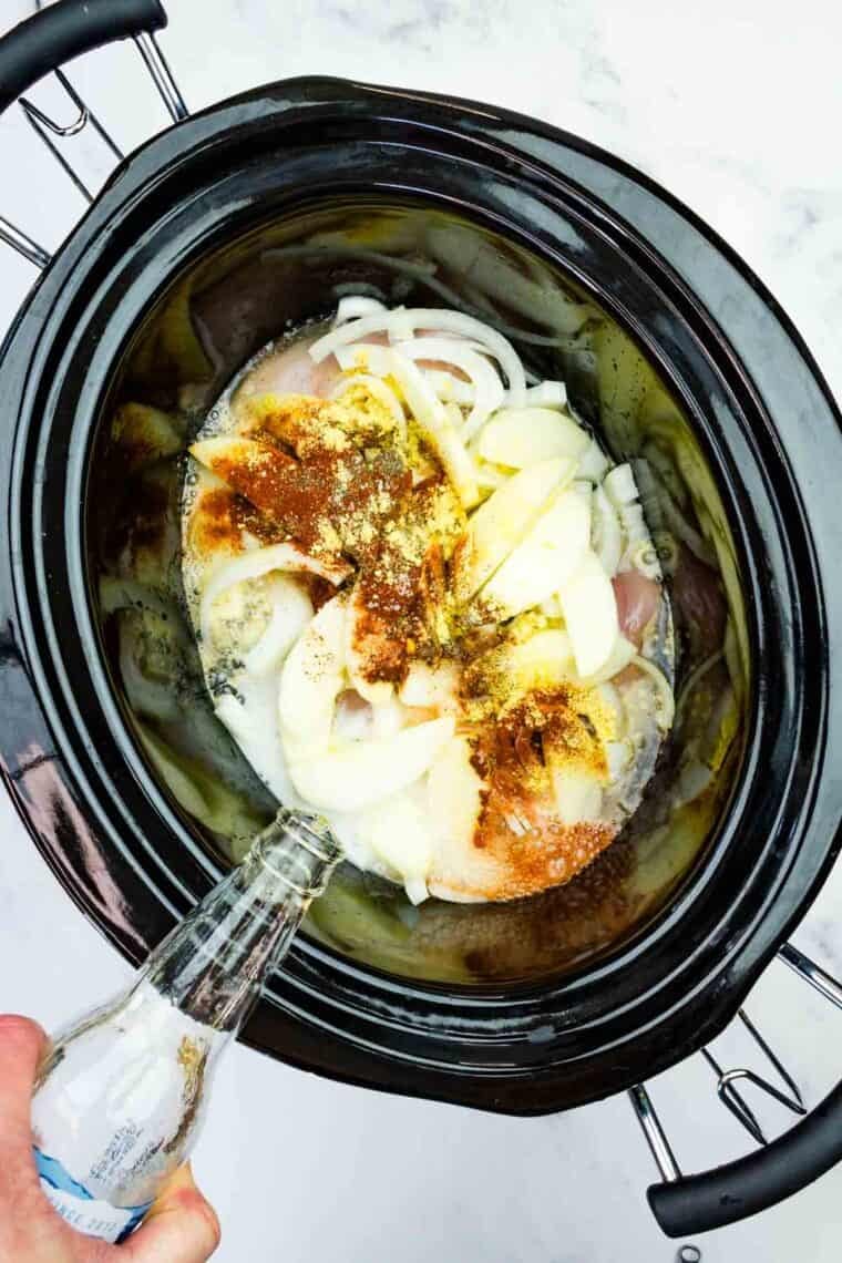 This easy slow cooker pulled chicken is simmered for hours with hard apple cider, apples, and onion. It's SO tender and ideal for sandwiches! Pouring hard apple cider into a crockpot loaded with chicken, apple slices, onion, and seasonings.