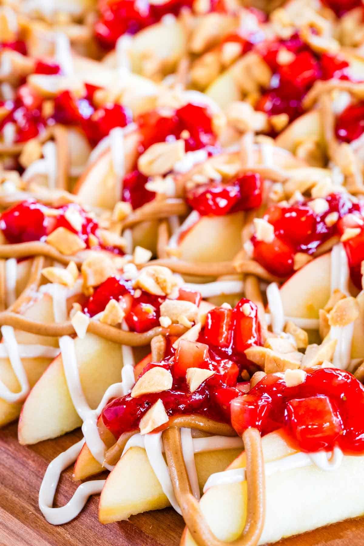 With apple slices instead of chips, no-bake apple nachos are topped with sweetened cream cheese, saucy strawberries, and peanut butter. Yum! Close-up image of apple nachos.