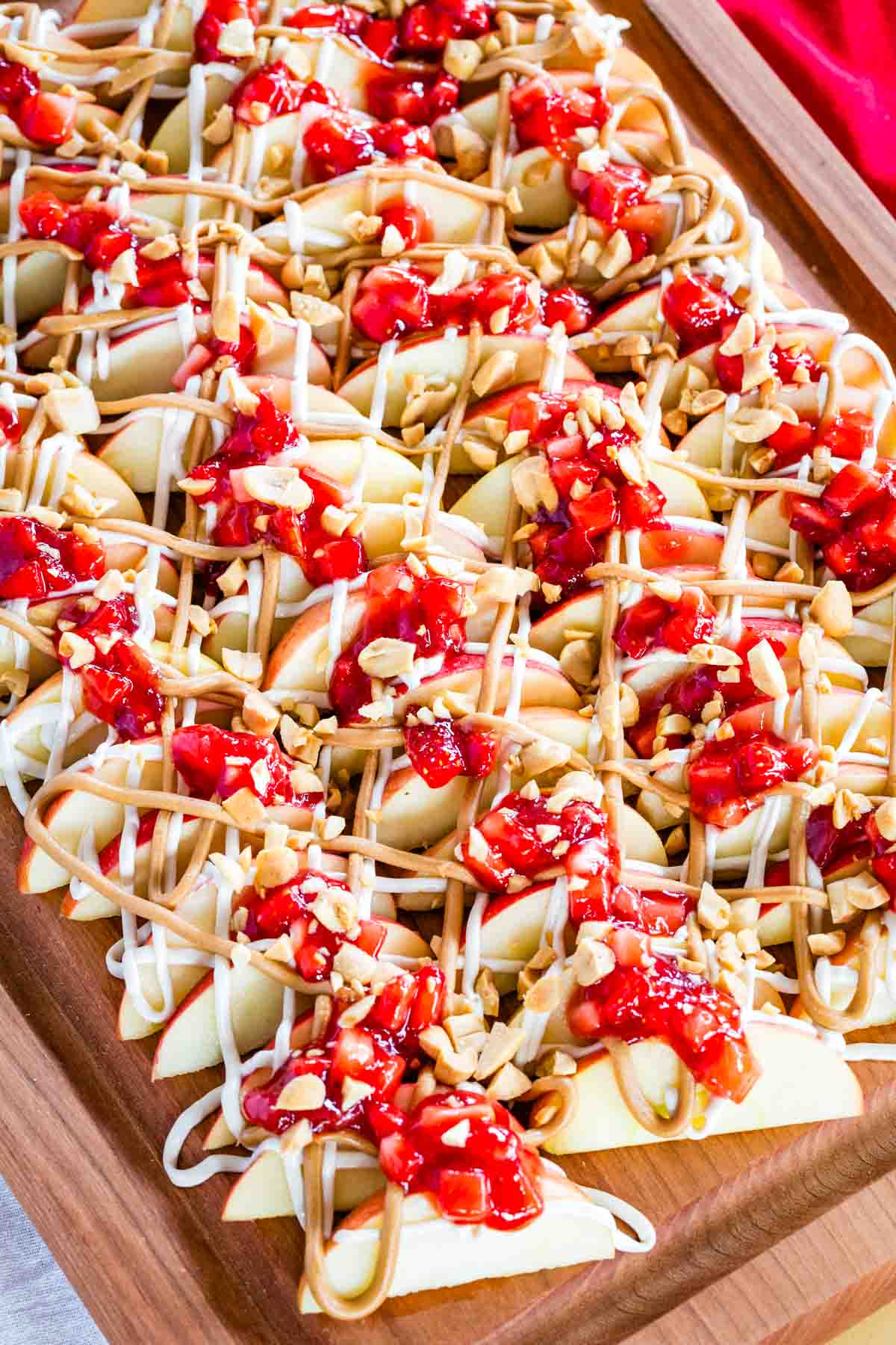 With apple slices instead of chips, no-bake apple nachos are topped with sweetened cream cheese, saucy strawberries, and peanut butter. Yum! Overhead image of apple nachos on a wooden platter.